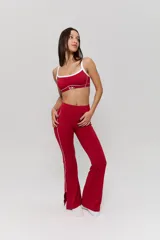 Conjunto deportivo compuesto por un top y un pantalón largo de corte acampanado, ambos en color rojo con detalles de líneas blancas. El top presenta breteles finos y el logo 'bk.' estampado en el frente. El pantalón cuenta con una línea lateral blanca y aberturas en el ruedo.