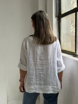 Blusa blanca de lino, con escote en V y tres botones frontales grandes de madera. Cuenta con mangas tres cuartos con presilla y botón para arremangar.