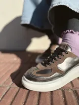 Zapatillas deportivas de cuero color peltre, con cordones negros y suela de goma blanca.