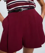 Short de sastrería color bordó, con pliegues delanteros, cierre interno y cinturón fino desmontable.