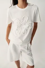 Camiseta blanca de algodón con cuello redondo, manga corta y detalle de flor en relieve bordada en el mismo tono.