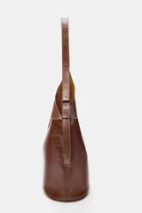 Bolso tipo saca de diseño asimétrico confeccionado en piel de color marrón. Cuenta con un asa de hombro ajustable y cierre mediante imán. Incluye una cartera con bolsillo extraíble en su interior.