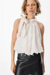 Blusa blanca sin mangas con cuello halter y lazo lateral. Confeccionada en tela de gasa con textura floreada en relieve.