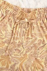 Pantalón de tiro alto con estampado paisley en tonos maíz y tierra, confeccionado en tejido fluido. Presenta cintura elástica con cordón ajustable y bolsillos laterales.