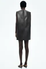 Vestido corto sin mangas en tejido revestido color negro con pespuntes trenzados, escote redondo y cierre oculto en la espalda.