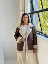Tapado de estilo aviador en color chocolate con interior y detalles de corderito en color beige. Presenta cierre frontal cruzado con botones, solapas amplias y puños con borde de corderito.