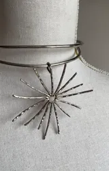 Gargantilla doble plateada con aro rígido y dije de sol con rayos texturados.