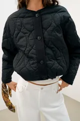 Cazadora corta acolchada de color negro, con cuello redondo, manga larga y cierre frontal con botones. Presenta un diseño de costuras geométricas y bolsillos laterales de vivo.
