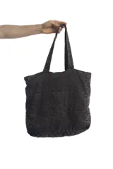Bolso tipo tote bag de denim negro con diseño acolchado de costuras cuadradas y doble asa superior. Cuenta con un parche ovalado frontal bordado con las letras "dl".