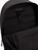 Mochila Tommy Hilfiger de diseño minimalista y silueta tipo domo en color gris oscuro. Cuenta con compartimento principal con cierre de cremallera, un bolsillo exterior frontal con solapa y cierre magnético, correas de hombro acolchadas y ajustables, y un asa superior. Presenta el logo de la marca en relieve en el frente y detalles distintivos.