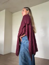 Ruana tejida de punto con hilo de algodón y lurex color bordó, de diseño amplio y caída asimétrica.