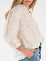 Blusa de broderie blanca con escote en V, mangas tres cuartos abullonadas y diseño holgado.
