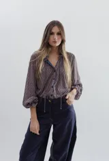 Camisa de tela liviana con estampado geométrico en tonos azul y bordó. Presenta cuello tipo isabelino con volados y lazos, mangas largas abullonadas con puños con volados y cierre frontal con botones metálicos.