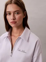 Buzo Calvin Klein de tejido french terry color lila claro, con cuello tipo polo y cierre de media cremallera. Cuenta con el logo de la marca bordado en el pecho y diseño de manga larga.
