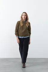 Sweater de tejido de punto color verde oliva, con cuello redondo y detalle de bordado floral sutil en el pecho. Presenta un corte relajado y mangas largas.