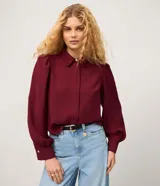 Camisa de crepé color bordó, con cuello inglés, mangas largas abullonadas con puños abotonados y cierre frontal oculto con botón diferenciado en el cuello.