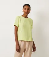 Blusa blanca de poliéster con cuello redondo, mangas cortas, cierre trasero en forma de gota, pequeñas aberturas laterales y acabados en pespuntes en las mangas y el cuello.