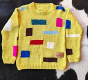 Buzo tejido a mano en lana 100% merino, color amarillo, con cuello redondo y diseño de bloques geométricos multicolores distribuidos por la prenda.