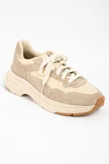 Zapatilla urbana de diseño chunky, confeccionada en una combinación de cuero liso y gamuza en tonos beige y arena. Presenta cordones al tono, suela de plataforma con relieve y detalle de marca grabado en el talón.