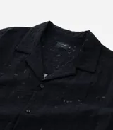 Camisa masculina negra de corte boxy, confeccionada en viscosa texturizada con efecto cutout. Presenta cuello solapa, manga corta y cierre abotonado frontal.