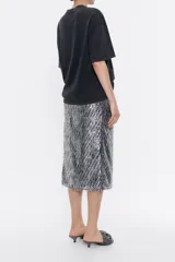 Falda midi plateada con lentejuelas y flecos en el ruedo, corte recto, cierre trasero con cremallera invisible y abertura frontal.