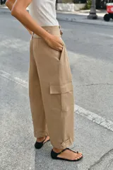 Pantalón de tiro alto estilo paperbag en color beige, con pinzas frontales y cinturón de la misma tela. Presenta bolsillos laterales tipo cargo con solapa y pernera ajustable con botones en el bajo.