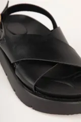 Sandalias negras de tiras cruzadas en símil cuero, con plataforma de 4cm de alto y tira ajustable con hebilla metálica.