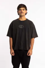 Remera de corte boxy fit, color negro con efecto lavado, de manga corta y cuello redondo. Presenta un logo bordado en el centro del pecho dentro de un óvalo.