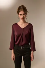 Blusa de satén color bordó con cuello en V y mangas tres cuartos. Presenta un diseño holgado con un pliegue central en el frente.