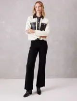 Chaqueta de corte boxy confeccionada en tejido de punto color crema, con detalles en cuero sintético negro en cuello, solapas, cartera central y bolsillos frontales. Presenta cierre frontal con botones metálicos plateados y costuras decorativas visibles.