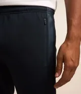 Pantalón deportivo de corte ajustado, color negro, con cintura elástica, cordón de ajuste, bolsillos laterales con cremallera, bandas laterales en contraste y cremalleras en los tobillos.
