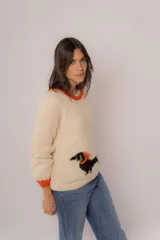 Buzo tejido a mano en lana merino, color crudo con diseño de perro salchicha en negro y detalles de costuras en color naranja en cuello y ruedo.