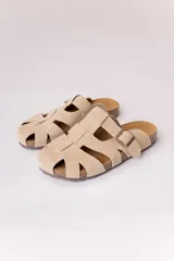 Zuecos de gamuza color beige, con diseño tipo sandalias romanas de tiras anchas entrelazadas, hebilla lateral metálica regulable y suela anatómica de corcho.