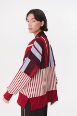 Buzo de tejido de punto con diseño de bloques de rayas verticales en colores rojo, verde, bordó y crema. Presenta cuello alto, corte oversize y terminaciones en rib en puños y ruedo.