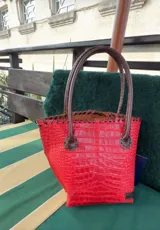 Cartera de cuero con textura crocco en color rojo, de silueta estructurada, manijas largas marrones y detalles de terminación artesanal en el borde superior.