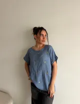 Blusa de manga corta y silueta holgada, confeccionada en símil gamuza color celeste, con delicados bordados florales distribuidos en la parte frontal y escote redondo.