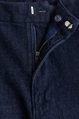 Jean de denim azul oscuro con tiro alto y corte acampanado, confeccionado con algodón elástico. Presenta bolsillos laterales al bies y cierre frontal oculto.