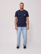 Remera color crema de manga corta con cuello redondo y bolsillo en el pecho con logo estampado de Rusty Shop Surf Services.