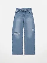 Pantalón de jean estilo wide leg con diseño de cintura cruzada y tiro bajo. Presenta un lavado azul medio con efecto desgastado y un detalle de rotura en la rodilla derecha.