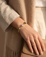 Pulsera de acero con baño de oro y malla tipo milanesa, con tres dijes circulares incrustados: uno de nácar, uno con circonias y uno de ónix negro.