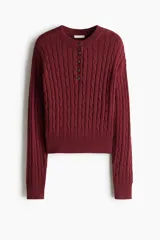 Buzo de punto trenzado en mezcla de algodón, con cuello redondo y tapeta frontal con botones. Presenta puños y bajo acanalados.