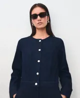 Mono largo de denim color azul oscuro, con cuello redondo, manga larga y cierre frontal de botones metálicos. Presenta corte recto y holgado en las piernas.