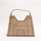 Cartera Xavielle de diseño estructurado trapezoidal en color beige, confeccionada en material sintético con efecto gamuza. Presenta detalles de perforaciones geométricas en los bordes y el centro, con un asa corta superior y cierre principal.