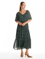 Vestido midi de gasa estampada con diseño de hojas, escote en V cruzado y mangas cortas fluidas. Presenta cintura elastizada con lazo ajustable y falda con volados escalonados que aportan movimiento. Incluye forro interno a tono.