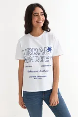 Remera blanca de manga corta de algodón, con cuello redondo y estampado frontal en color azul con texto y diseño gráfico.