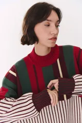Buzo oversize de tejido de punto con diseño de bloques y rayas verticales en colores rojo, verde, bordó y crema. Presenta cuello alto tejido y terminaciones en rib en puños y ruedo.