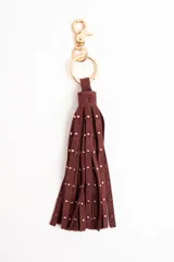 Charm para bolso compuesto por flecos de cuero sintético en color bordó, decorado con pequeñas tachas metálicas doradas y herrajes a tono.