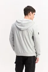 Campera de algodón gris melange con capucha, cierre frontal completo y bolsillos laterales. Cuenta con un parche rectangular negro con inscripciones en la manga y cordones ajustables para la capucha.