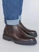 Botín tipo Chelsea de cuero color marrón oscuro, con paneles laterales elásticos y suela de goma dentada. Diseño clásico con tirador trasero.