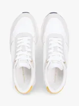 Zapatillas de estilo runner de Tommy Hilfiger, confeccionadas en una mezcla de cuero y textil en color blanco con detalles en gris claro y un panel amarillo en el talón. Presentan cordones blancos y suela de goma con base oscura.